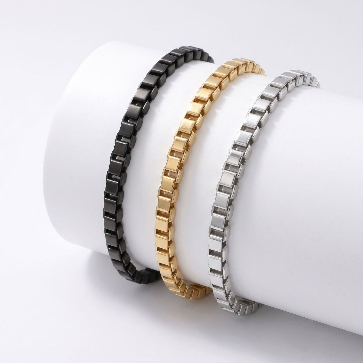 Gold, siyah ve gümüş üç köşeli arnavut bileklik beyaz silindir üzerinde yan yana