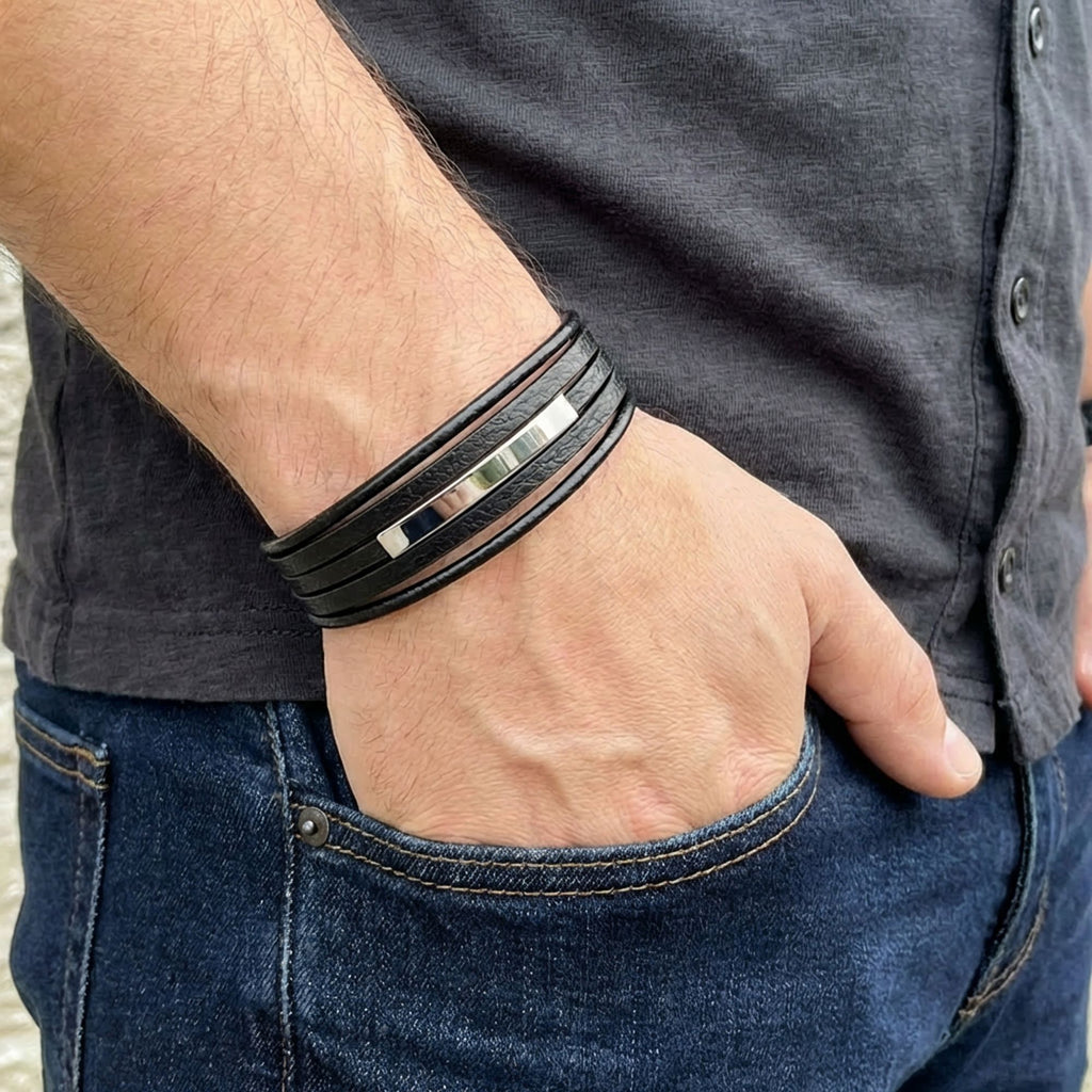 Cebinde eli duran erkeğin bileğinde katmanlı siyah deri ve parlak çelik plaka